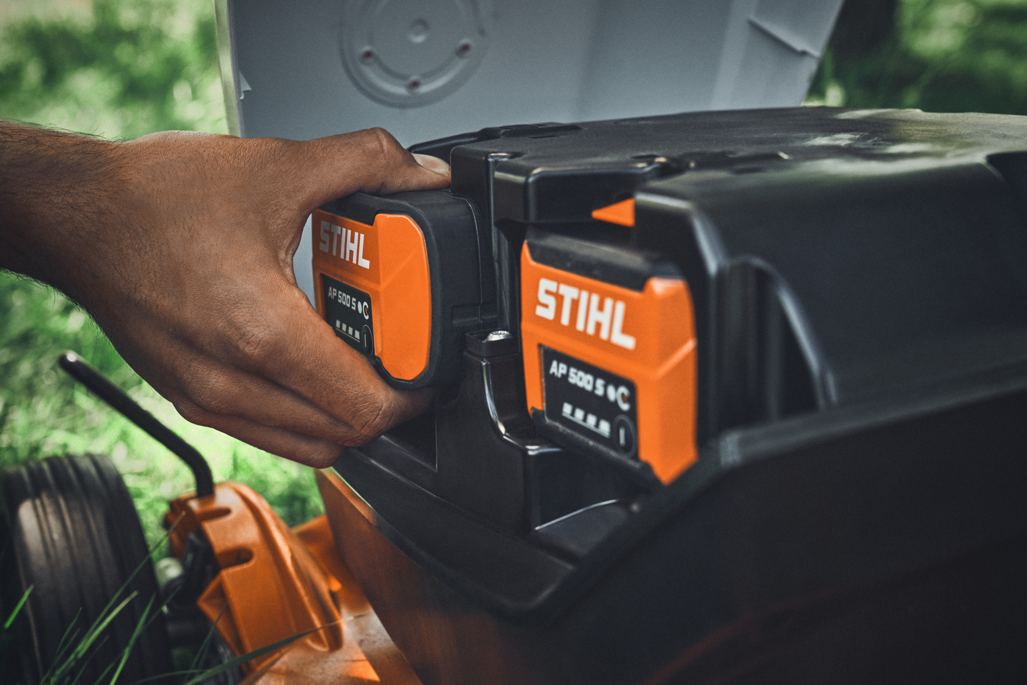 A person inserting a STIHL AP 500 S battery into a STIHL battery lawn mower